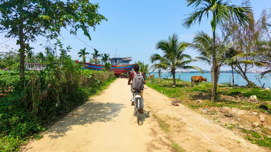 Riding a bicycle along a quiet paved road surrounded by small vegetable plots and fishing households on Cam Kim Island.