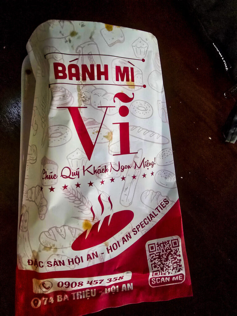 A printed paper wrapper from a famous local Banh Mi stall in Hoi An, displaying the menu and stall details.