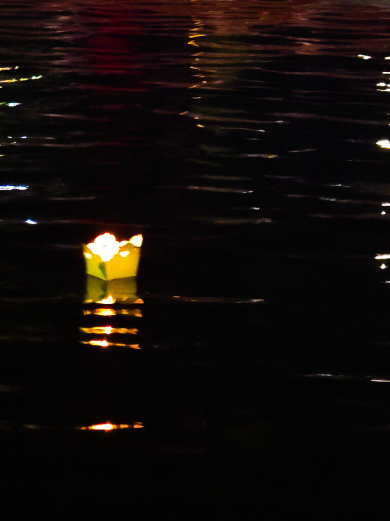 A close-up of a lit candle inside a colorful paper lotus lantern floating on the dark surface of the Thu Bon River.