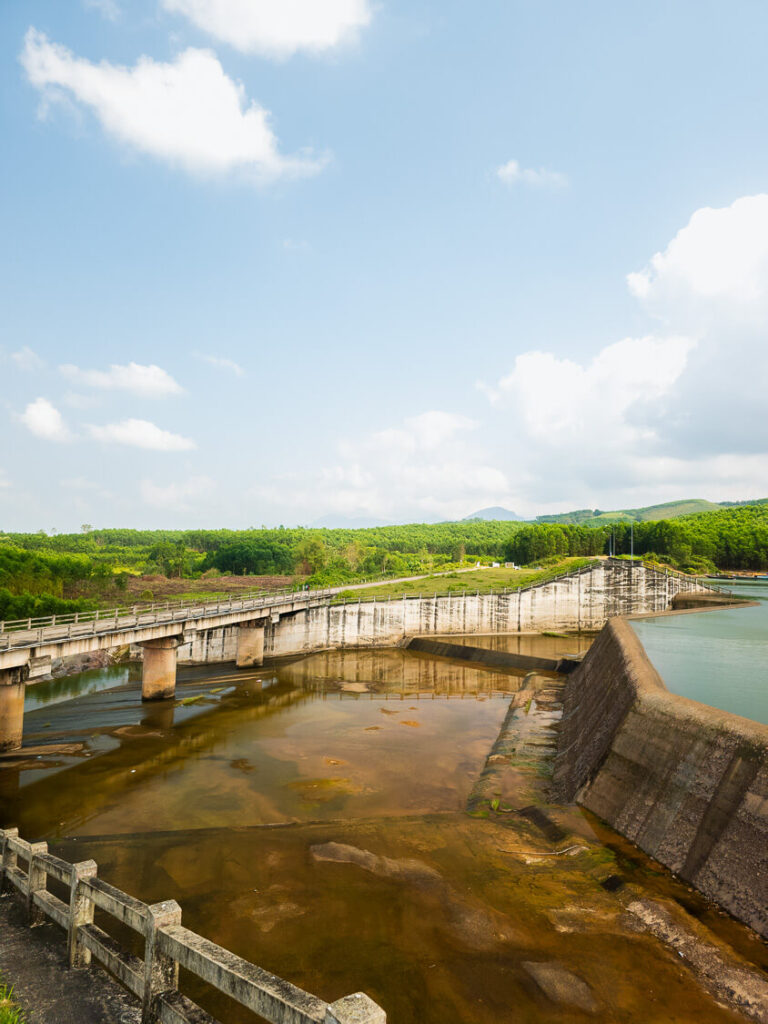 Wide view of Khe Tan Reservoir featuring a bridge in the foreground and calm water stretching out behind it.