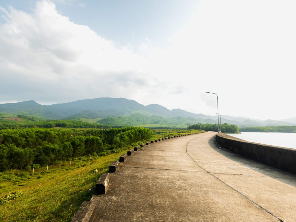 Wide landscape shot of the still water at Khe Tan Reservoir framed by the distant mountains of Quang Nam province.