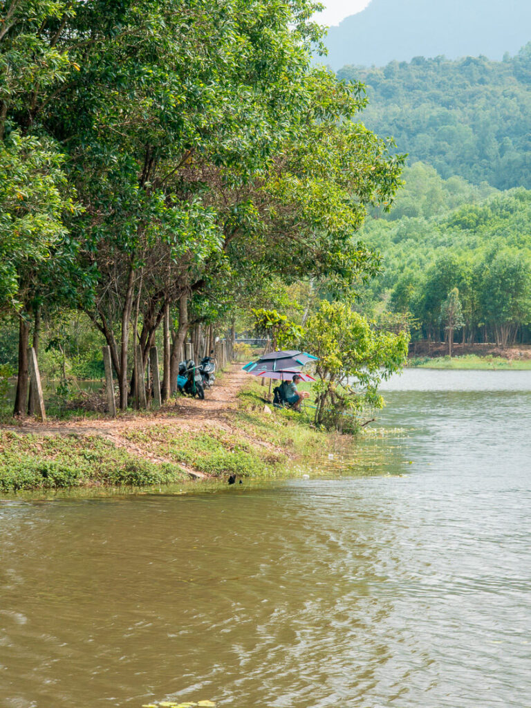 A local Vietnamese fisherman sitting quietly by the calm waters of a lake in the countryside near Hoi An.