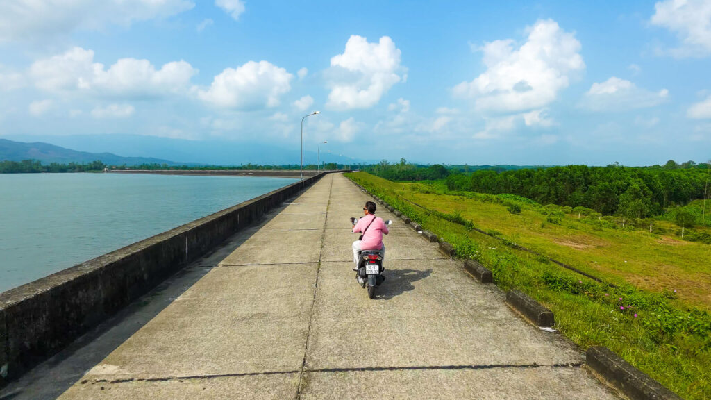 Vishal riding a scooter along the empty paved road hugging the edge of Khe Tan Reservoir.