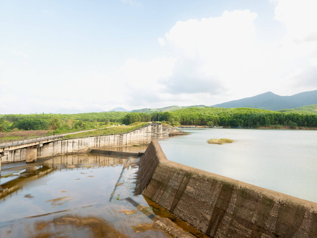 A wide landscape shot of the still waters and green hills surrounding the peaceful Khe Tan reservoir outside Hoi An.