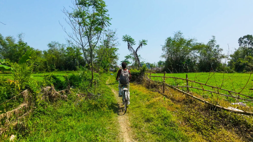 A traveler riding a bicycle down a quiet residential street in a rural Vietnamese village.