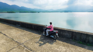 A traveler sitting on a rented scooter near a calm lake in Hoi An, demonstrating how to get around Vietnam independently.