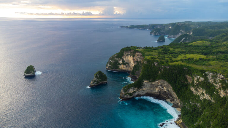 Aerial drone view of a beautiful sandy beach and rugged green cliffs in Bali, the ultimate destination when traveling from Jakarta to Bali.