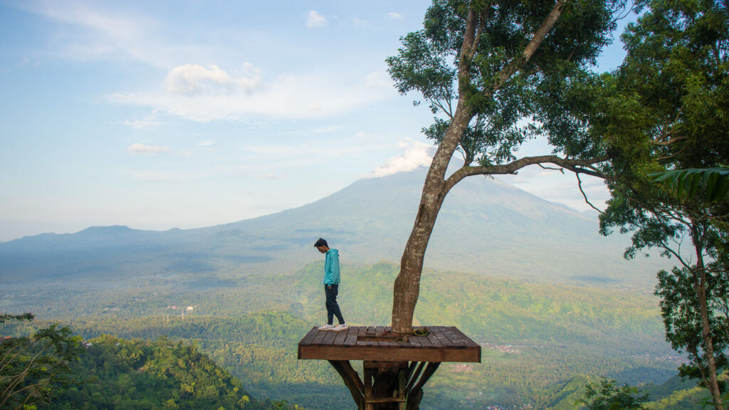 How to Plan a Trip to Bali 2026: The Ultimate Regional Travel Guide 1 A traveler standing on a wooden tree platform at Lahangan Sweet with the massive peak of Mount Agung in the background.