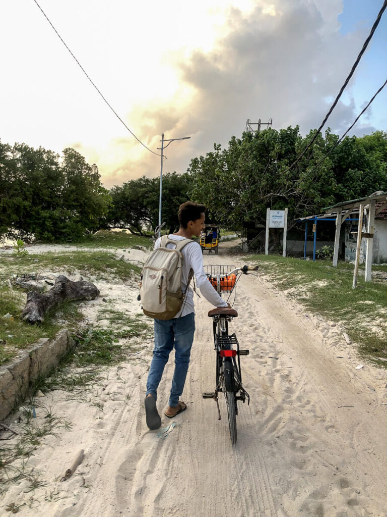 How to Plan a Trip to Bali 2026: The Ultimate Regional Travel Guide 8 A traveler pushing a bicycle along the white sand beach of Gili Trawangan with clear turquoise ocean water in the background.
