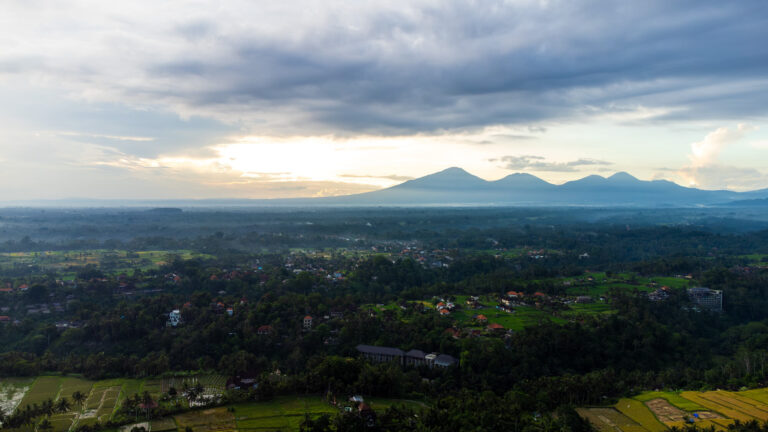Aerial drone view of lush green rice terraces with a towering volcano in the background, the beautiful final destination on a Surabaya to Bali trip.