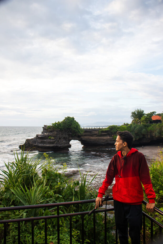 How to Plan a Trip to Bali 2026: The Ultimate Regional Travel Guide 2 A person standing on the rocky shoreline with the famous Tanah Lot sea temple resting on a rock formation in the background.