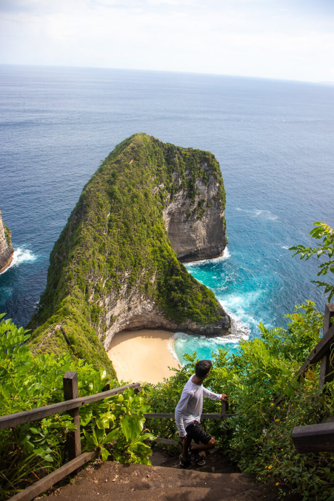 How to Plan a Trip to Bali 2026: The Ultimate Regional Travel Guide 5 A traveler carefully walking down the steep, narrow cliffside stairs leading to Kelingking Beach on Nusa Penida island.