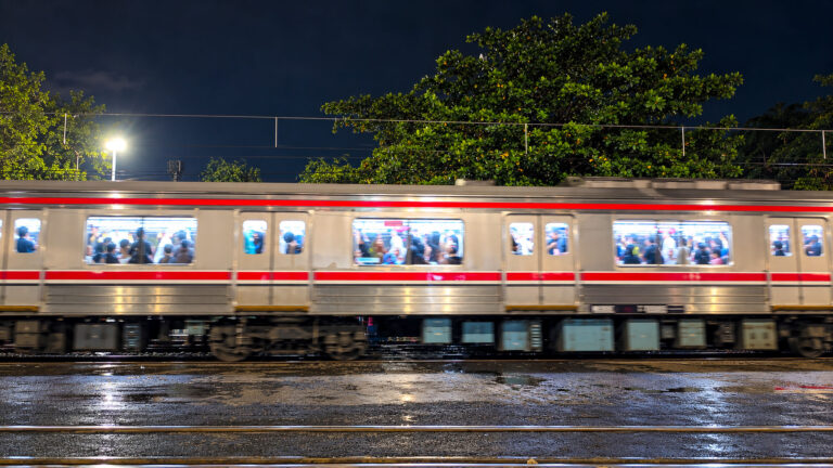 A fast-moving train blurred in motion leaving a brightly lit Yogyakarta station at night, representing the journey from Yogyakarta to Surabaya.